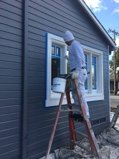 A painter on a ladder finishing exterior window trim